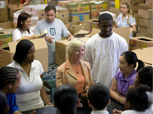 A woman talks to a group of students in a warehouse of boxes.