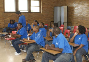 A group of young people in matching blue t-shirts sit in a classroom.