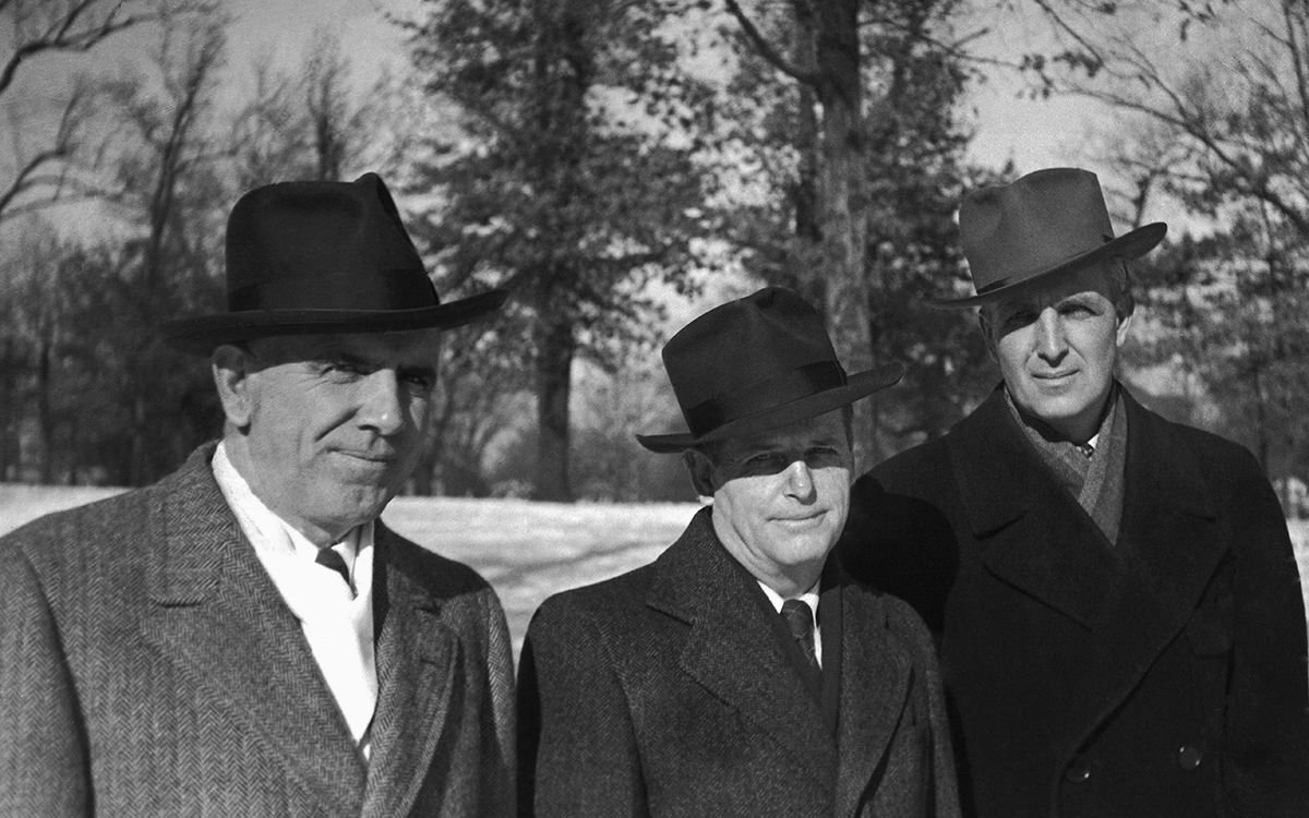 An old black and white photo shows three men outdoors wearing stylish hats and winter coats.