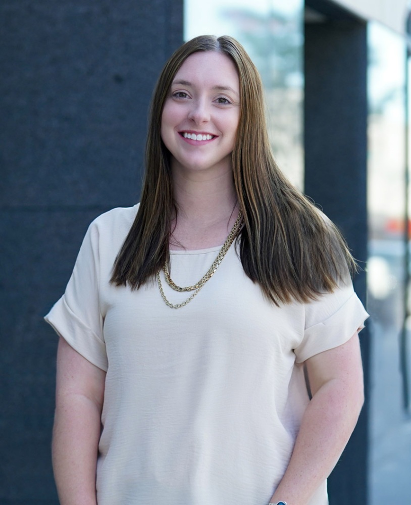 A woman stands on a sidewalk as she smiles at the camera.