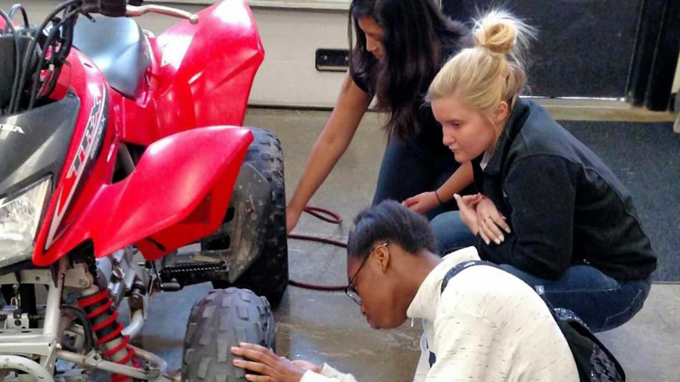 A group of students change a tire on an all-terrain vehicle.