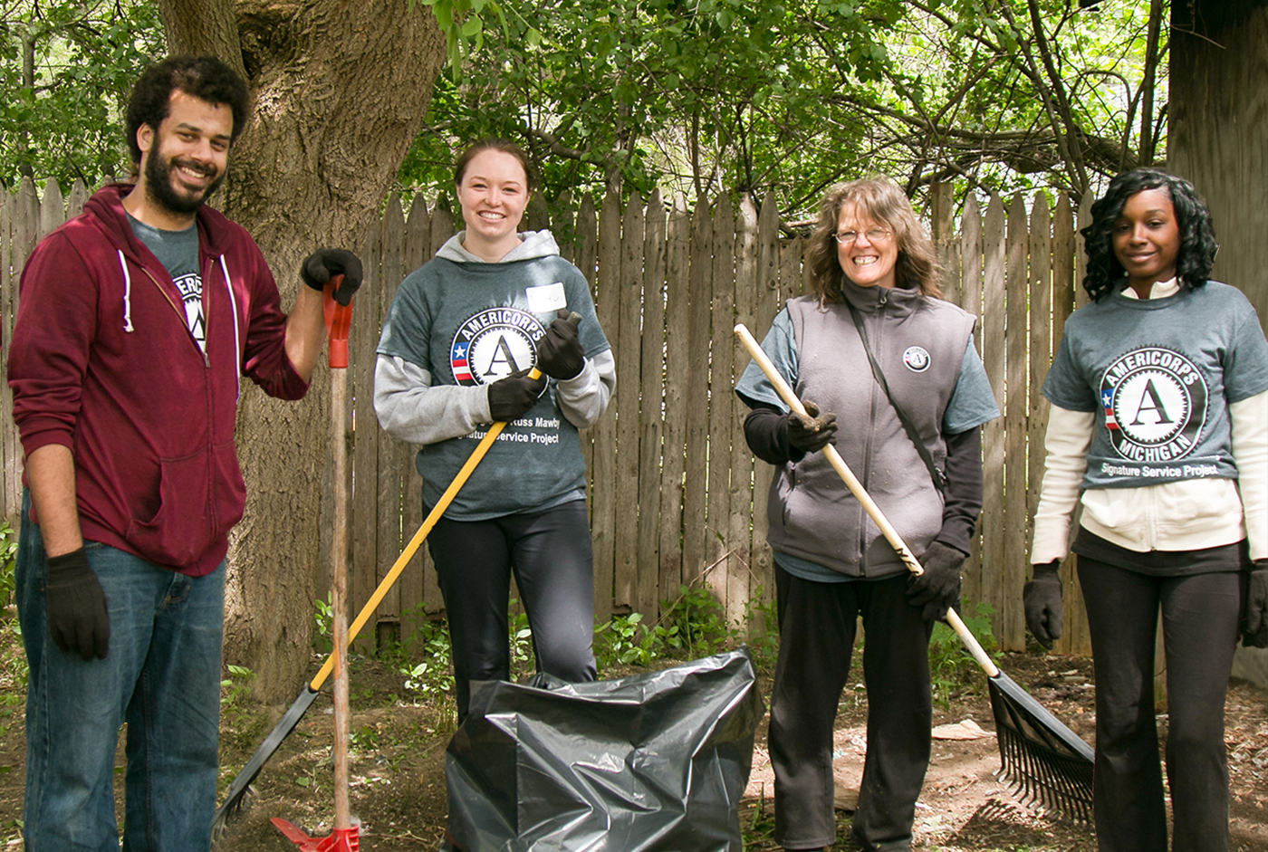A group of four AmeriCorps members hold rakes as they clean up a yard during a Day of Service.