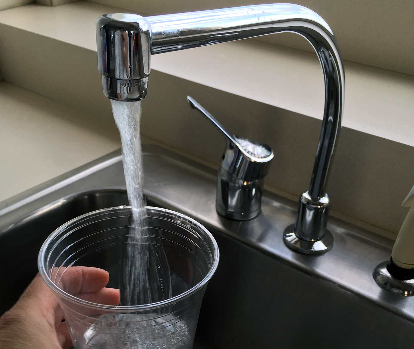A hand is shown filling up a clear plastic cup under a water faucet.