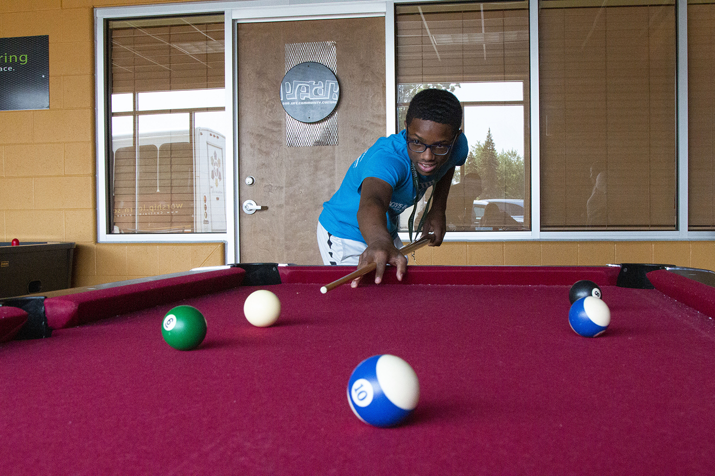 A young man leans across a billiards table with his stick as he is aiming to take a shot.