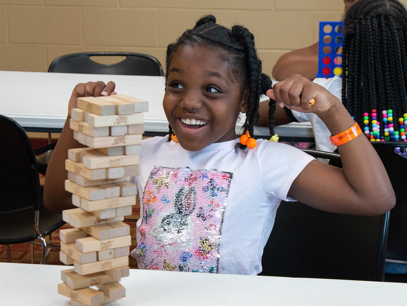 Young girls raises her fists in triumph after successfully removing a game peace from the base of a Jenga game tower and while not toppling it to the table.