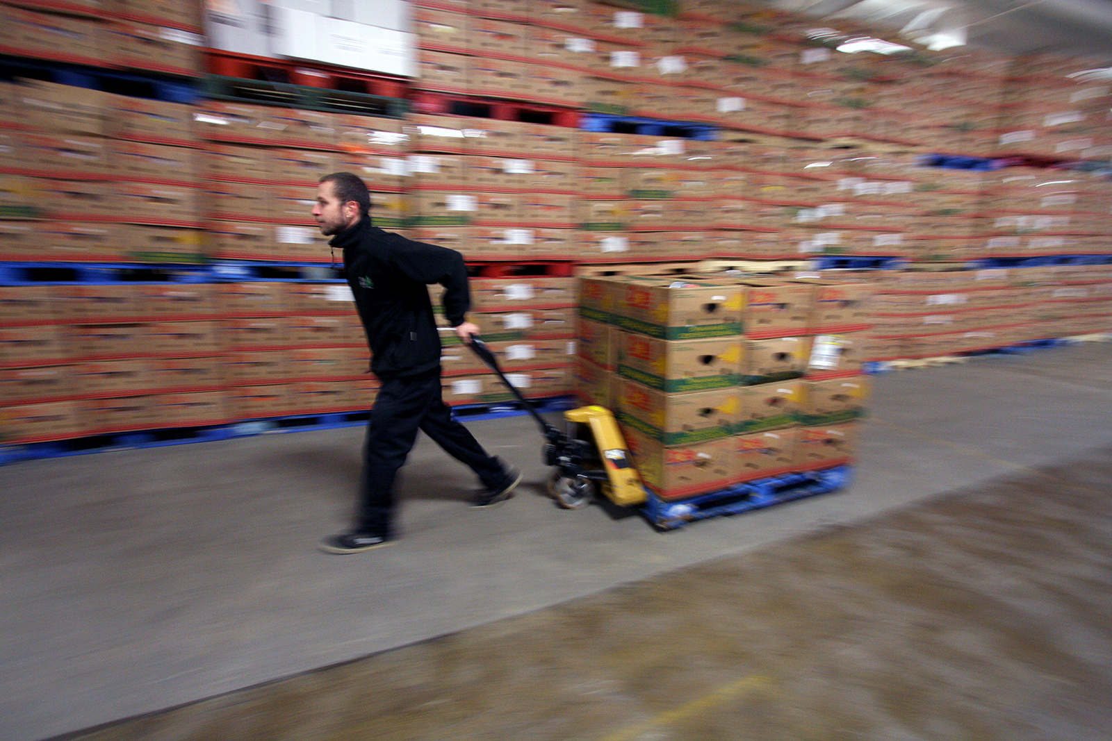 A man drags a palette through a box-lined warehouse.
