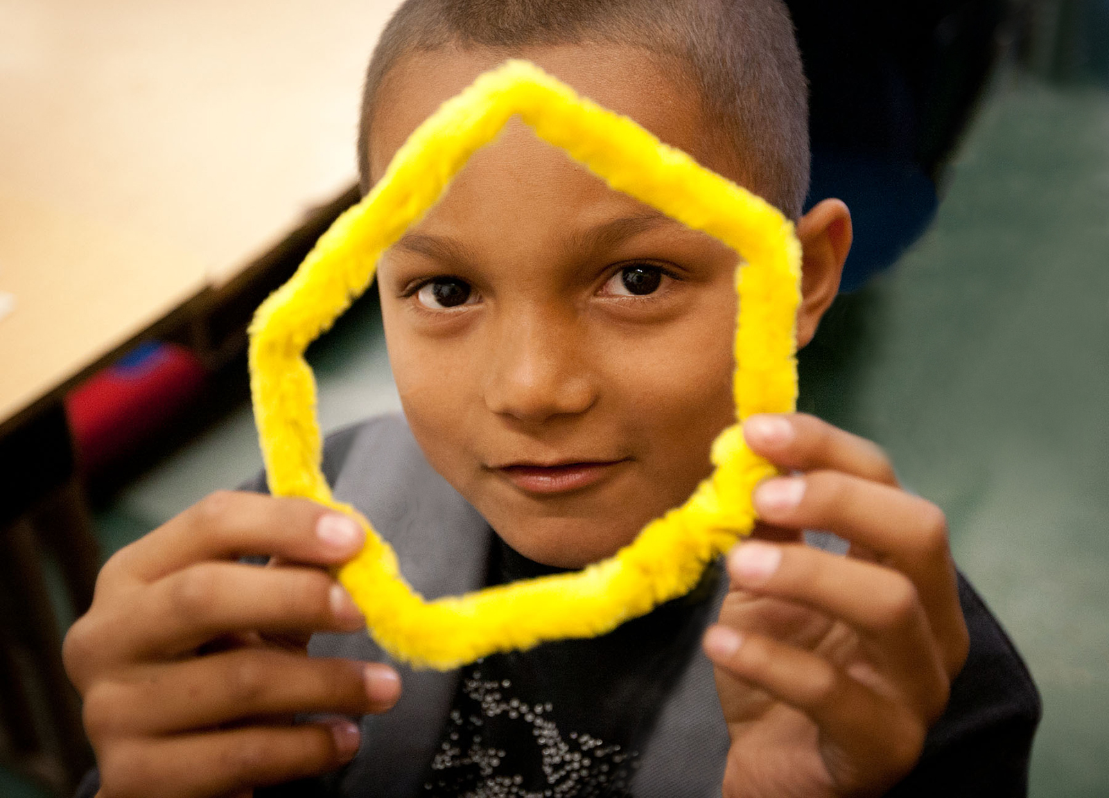 Young boy holds up and shows off a bright-yellow, fuzzy pipe cleaner he formed into a hexagon shape.