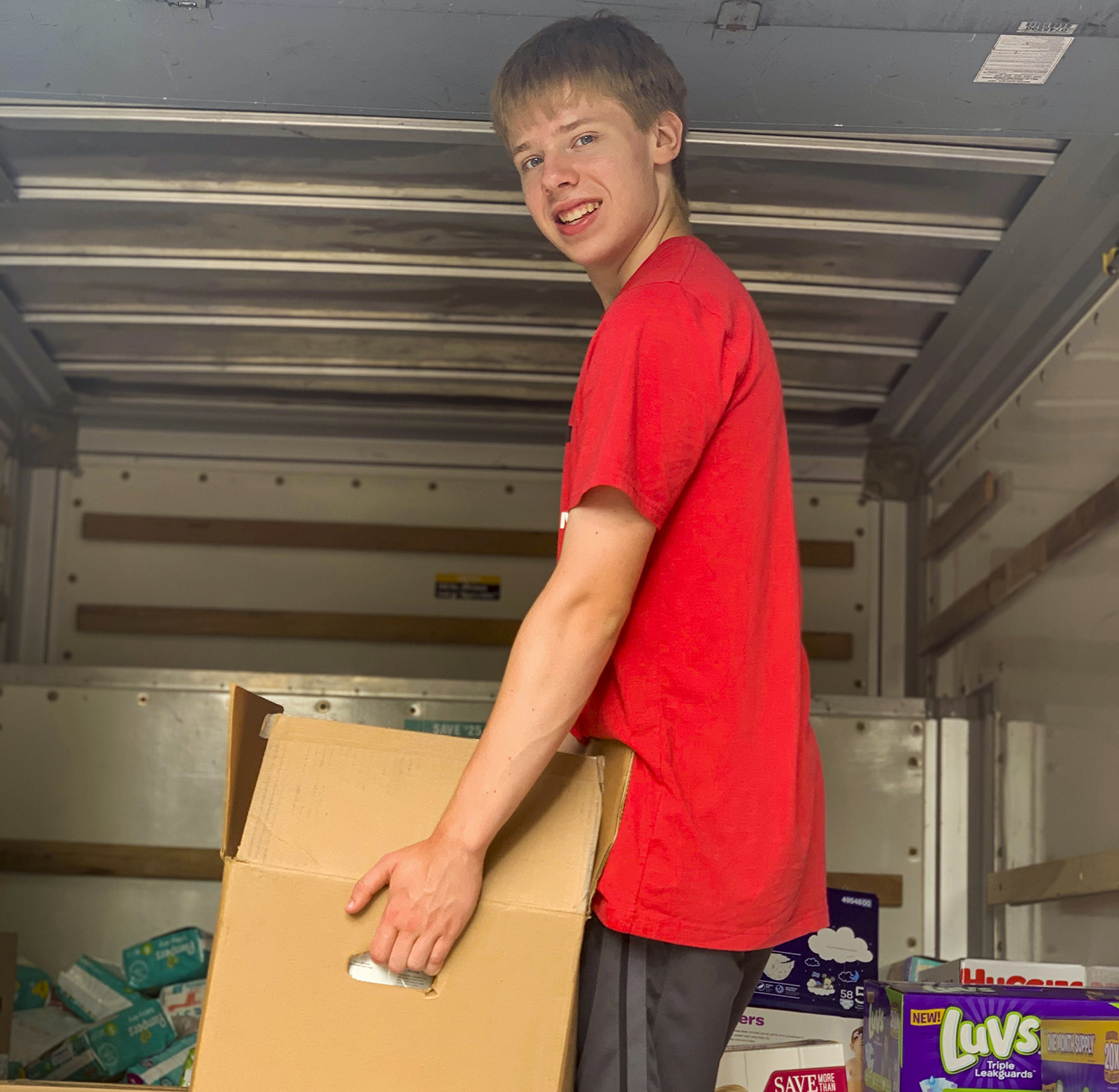 Young man in the back of a small cargo truck loads in baby diapers to be distributed in the area.