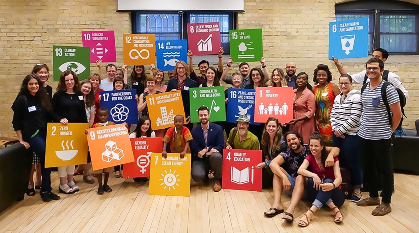 A large group hold colorful signs referencing the SDGs.