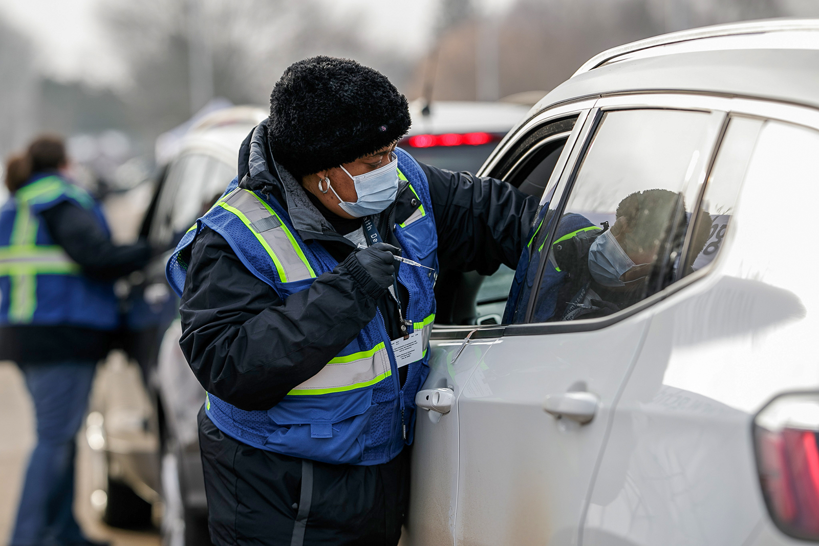 A Genesee County Health Department nurse reaches into the car window of a patient and is preparing to administer a COVID-19 vaccine into the arm.