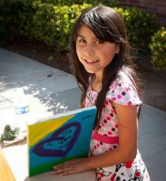 Young girl attending an afterschool program proudly displays her work of art, a painting with a hear around the words "I love you mom."