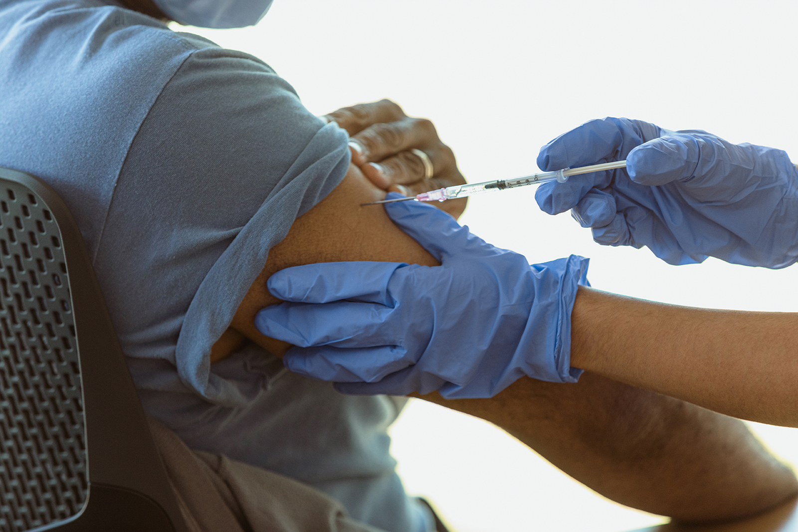A man holds an arm and watches as a nurse administers a vaccine.