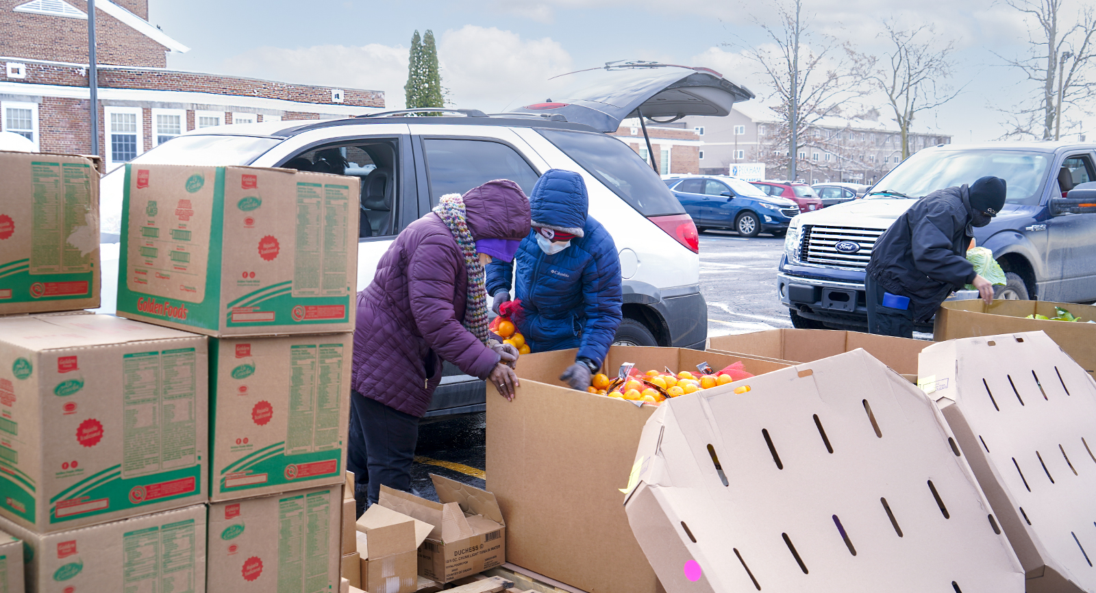 Volunteers, dressed warmly, distribute food to people lined up in cars in the parking lot of the Help Center at Bethel United Methodist Church in Flint, Michigan.