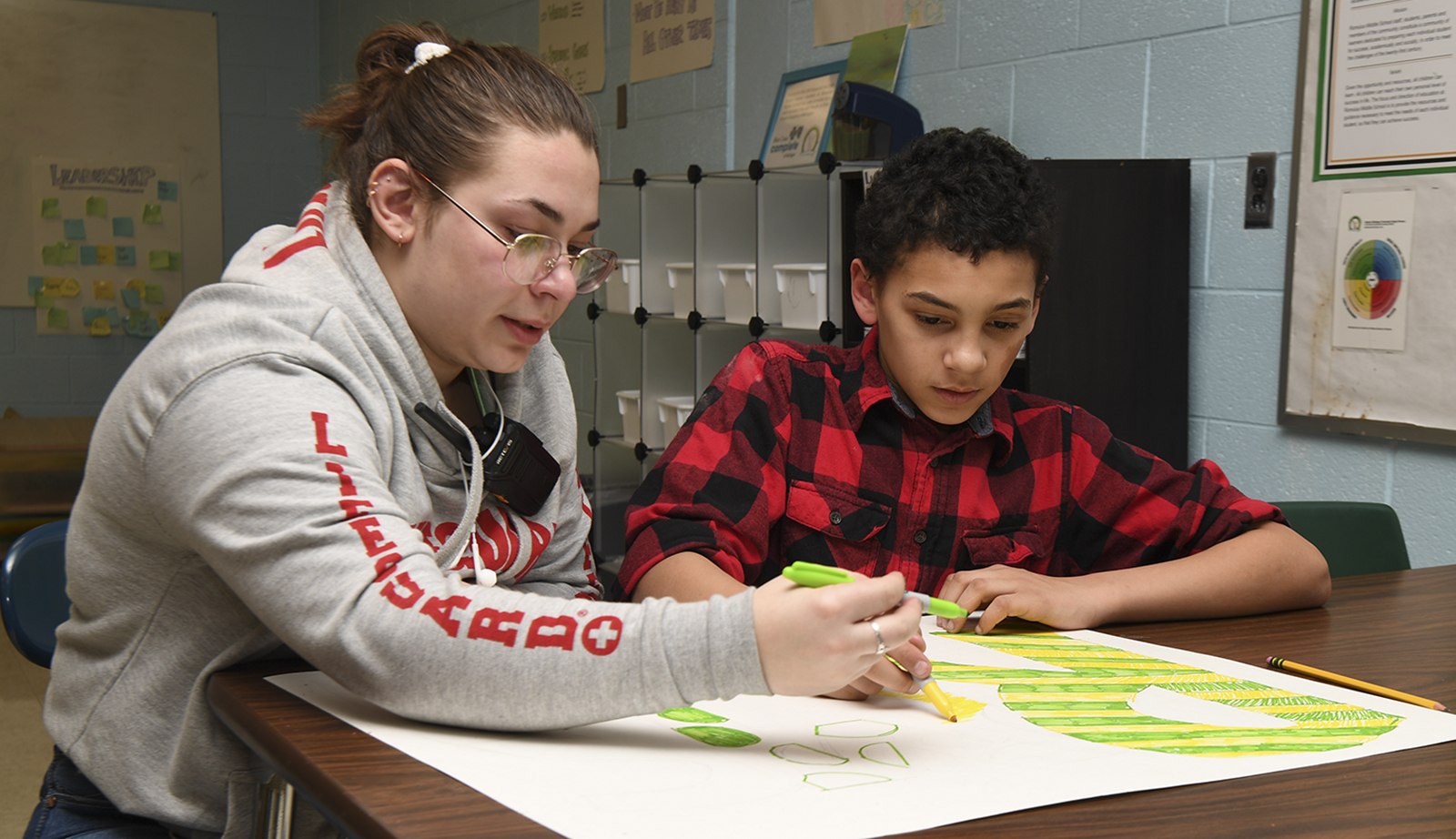 A college student helps a student create a poster.