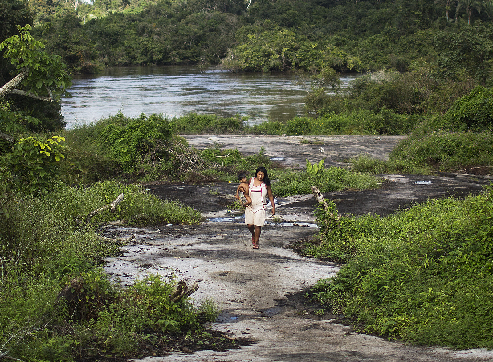 A woman holds her child while walking near a tributary of the Xingu River.
