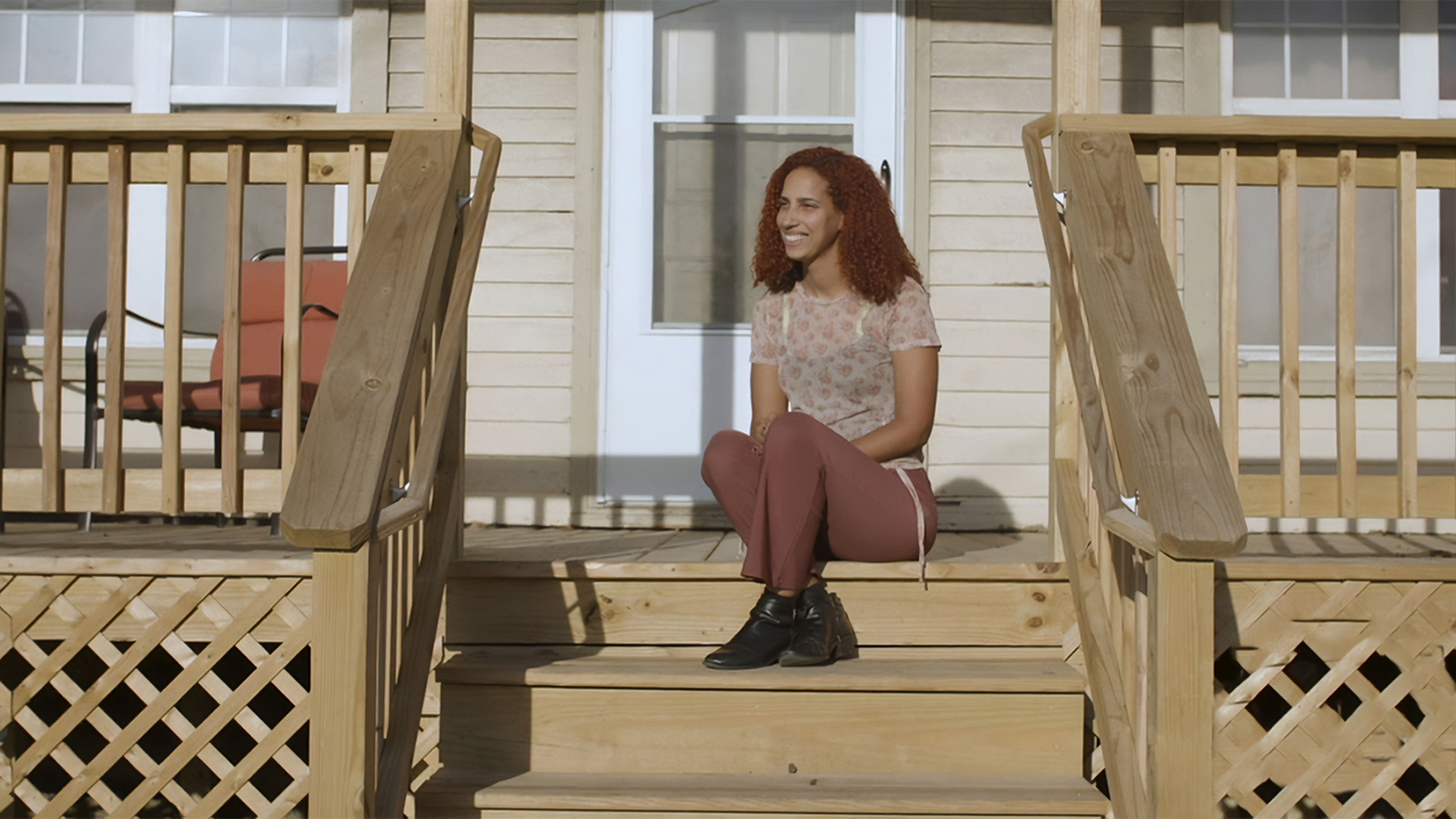 A smiling woman sits on her porch.