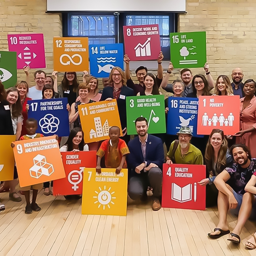 A large group pose in an office space with brightly colored signs indicating the sustainable development goals.