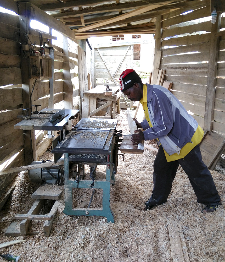 A man stands in a pile of sawdust while woodworking in an shed.