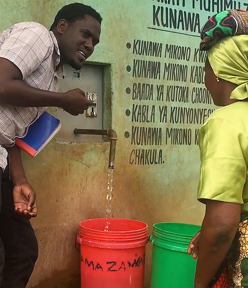 Two people fill brightly colored large buckets with water at a public spigot.