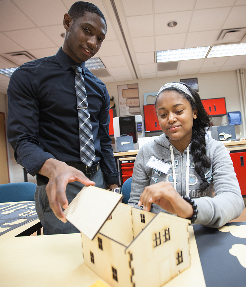 Two high school students put together the pieces of a house that was made on a laser cutter.