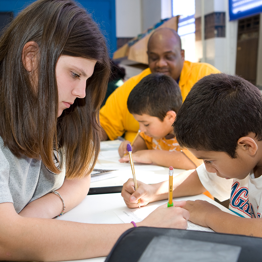Two students and an AmeriCorps member sitting at a table are focused on writing papers.