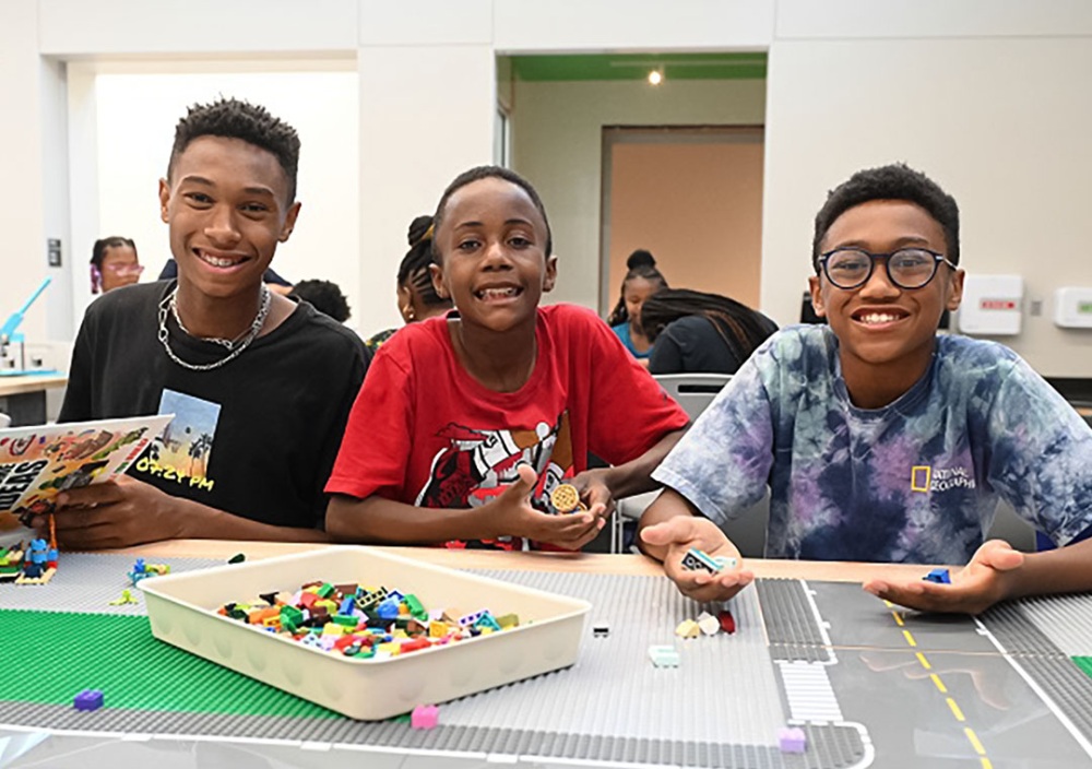 Three boys sit at a table working on Lego projects.