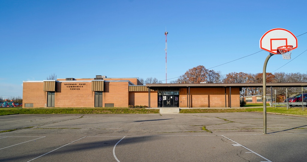 Image of a brick building with a basketball court in front of its doors.