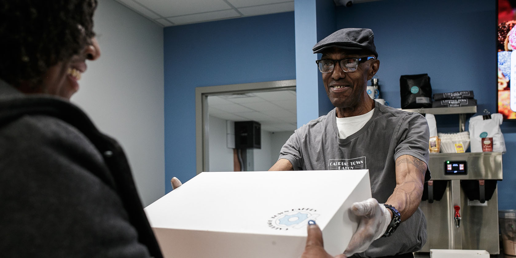 A sales associate hands off a boxed order of doughnuts at Carriage Town Bakery.