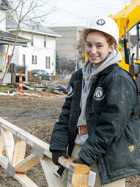 AmeriCorps members carry a ladder through a construction site.