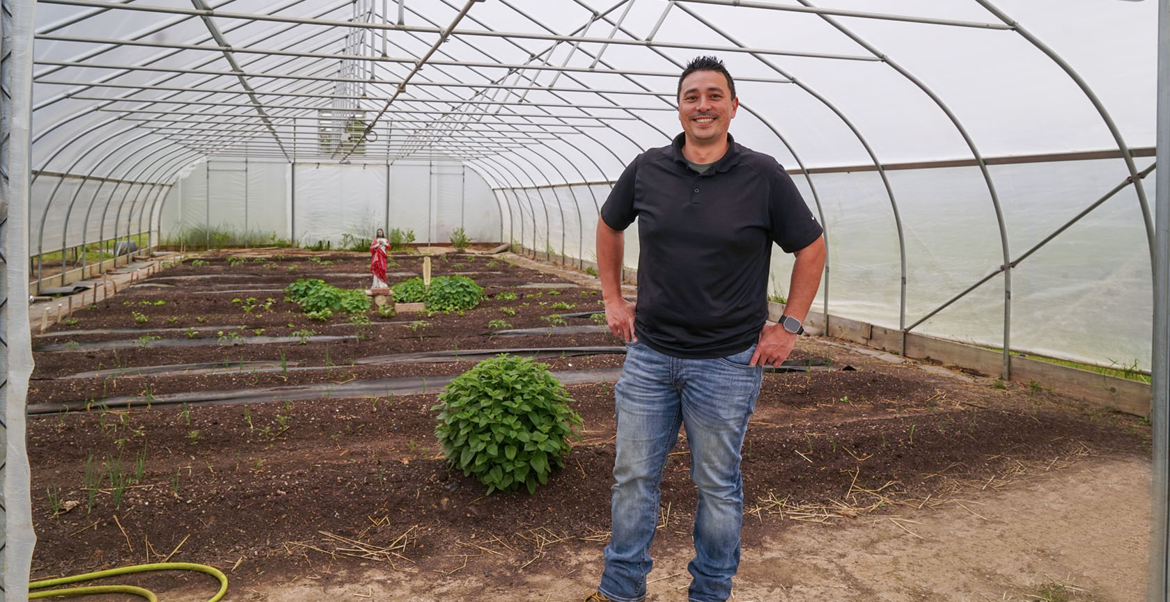A man stands at the entrance of a hoop house in the spring.