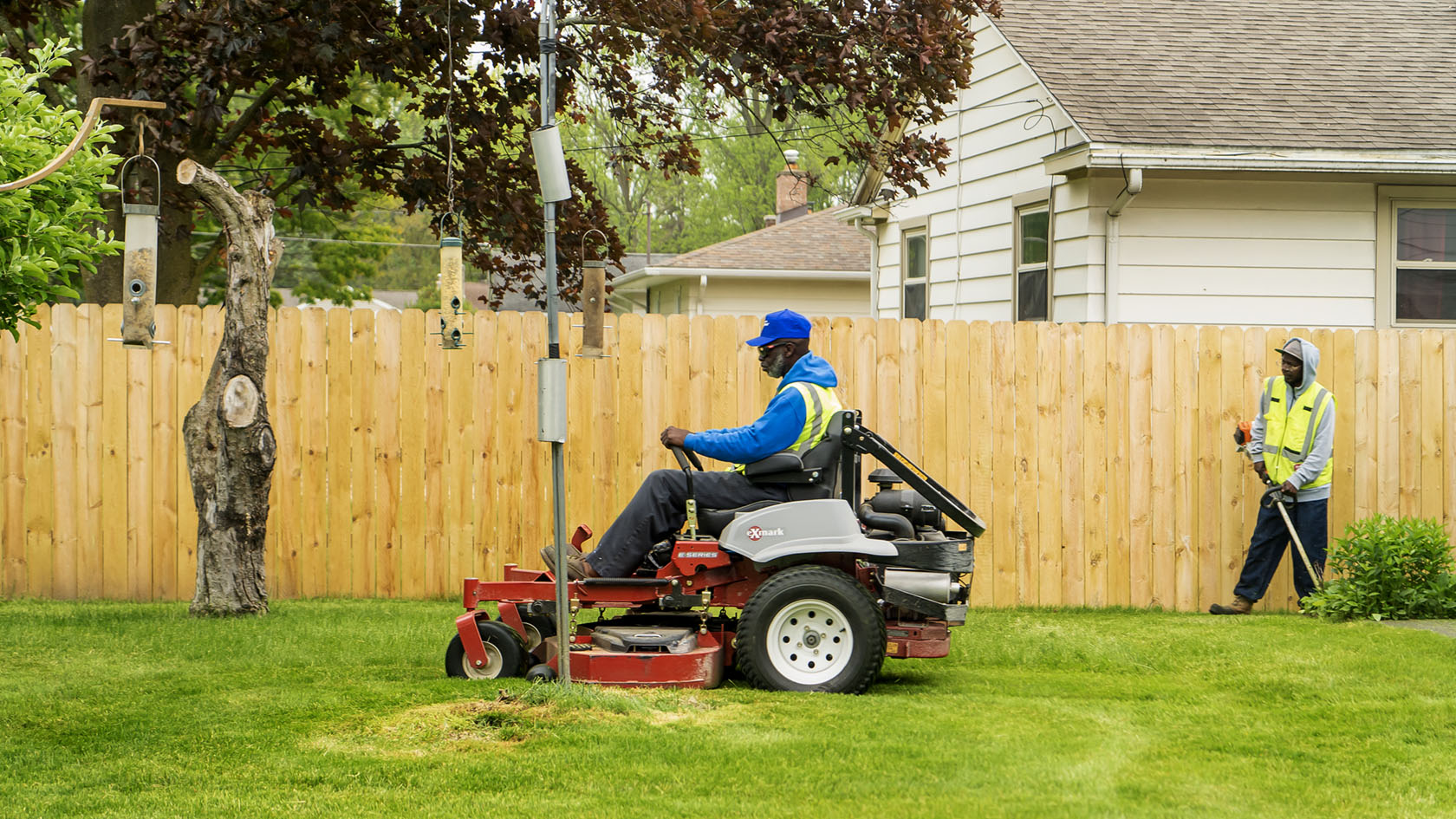 Two men mow a residential home that belongs to an elderly couple.