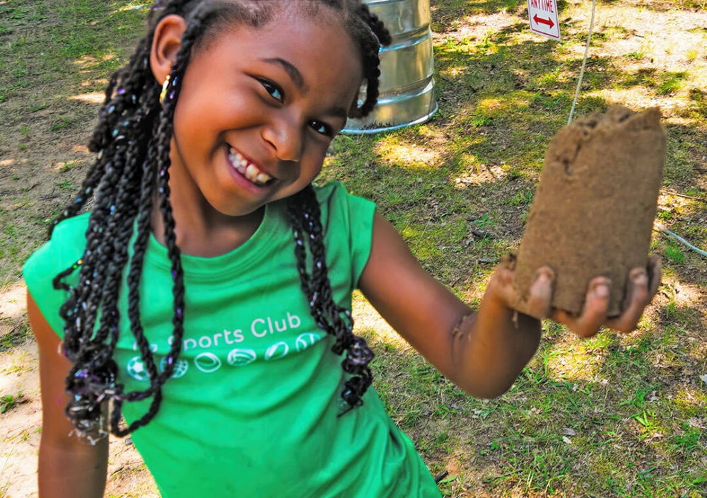 A young girl holds sand art in the shape of a small bucket.