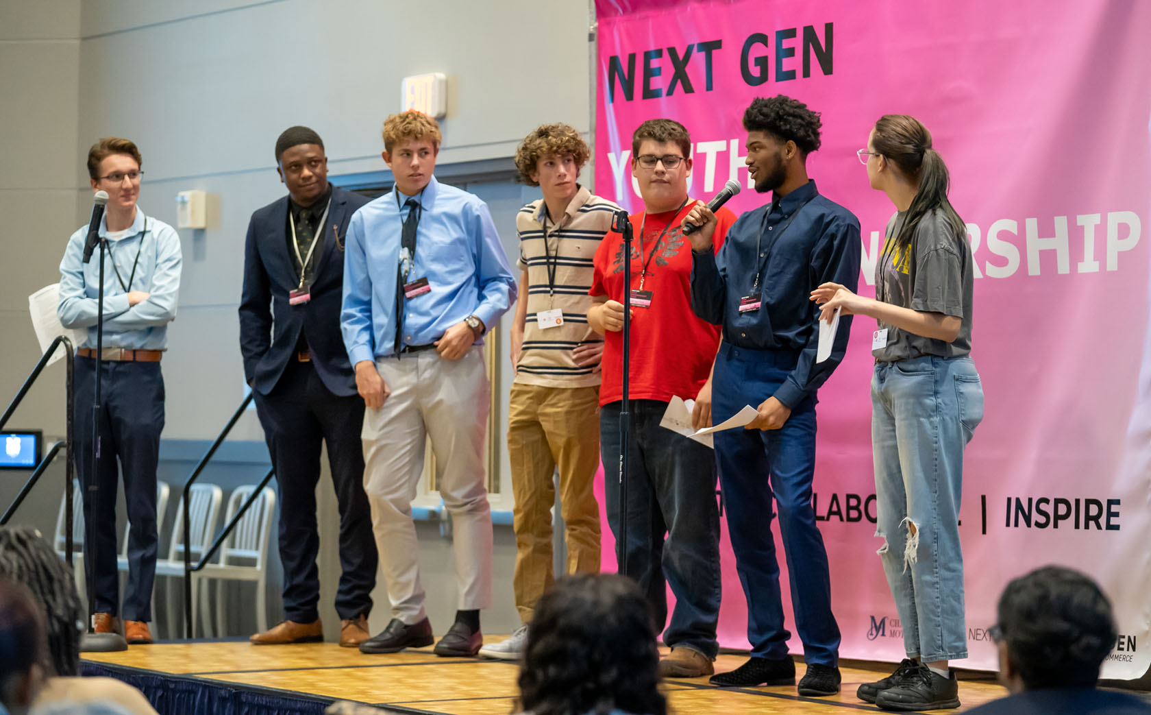 Genesee County high school students stand on the stage with their mentors as they make their pitch to judges at the hackathon.