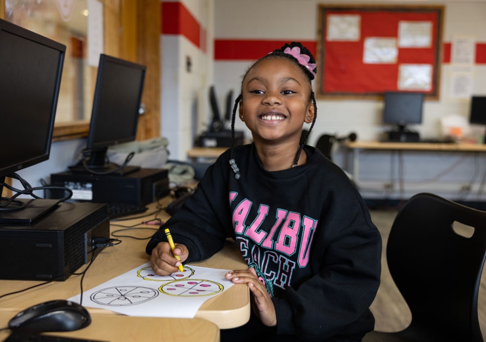 Young child drawing and smiling at camera.