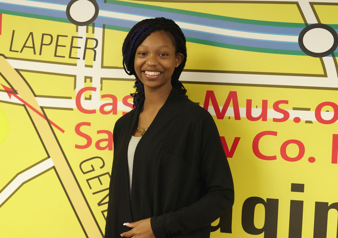 A young high schooler stands in front of a map as she poses for the camera.
