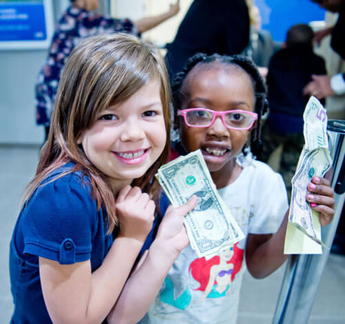 Two young girls hold dollar bills they will use to open a savings account.