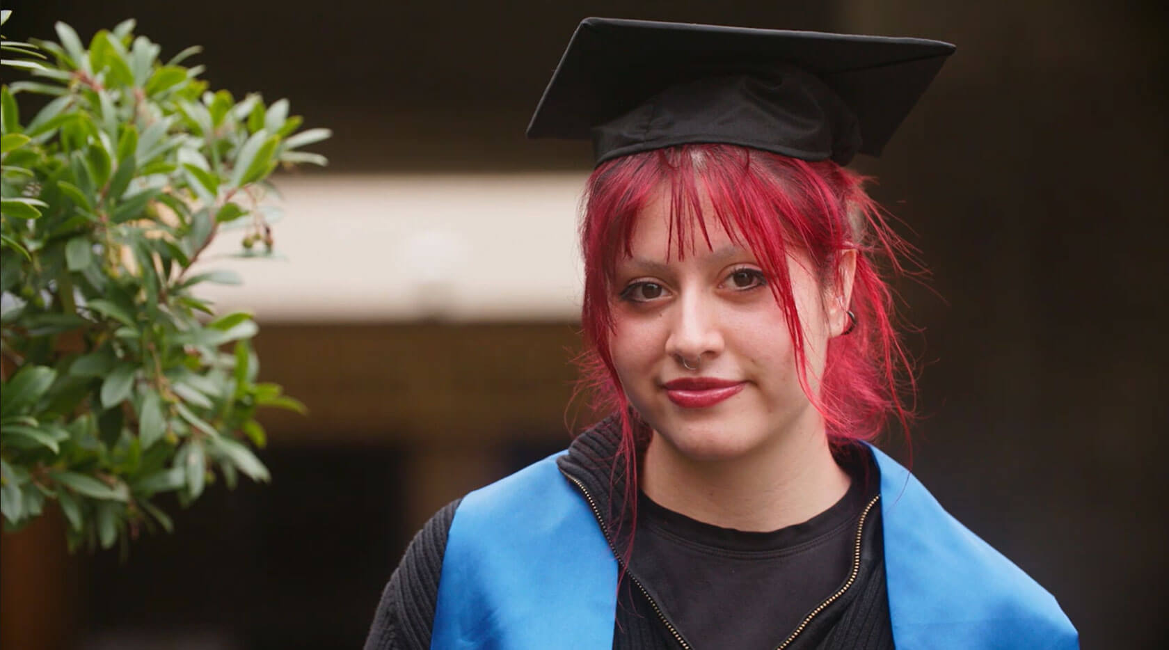 Young woman with red hair poses in her high school graduation cap and gown.