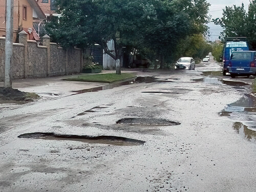 A wet, paved street is littered with potholes.