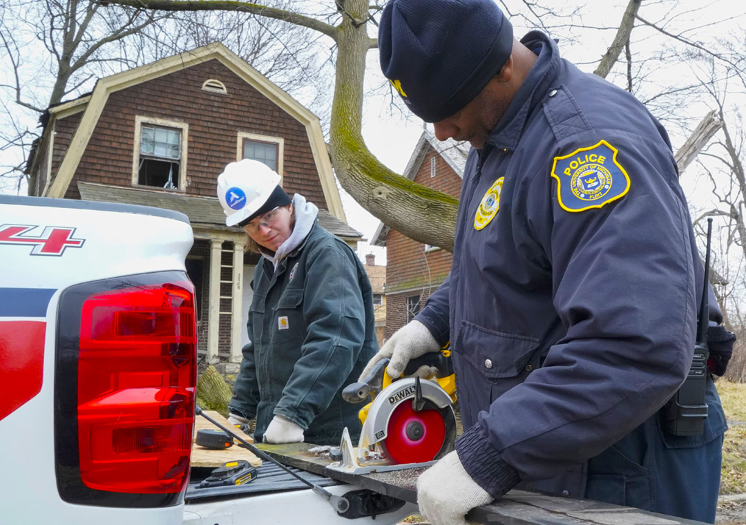 Young AmeriCorps NCCC service member works with a University of Michigan- Flint police officer to cut wood for boarding up a home in Flint.