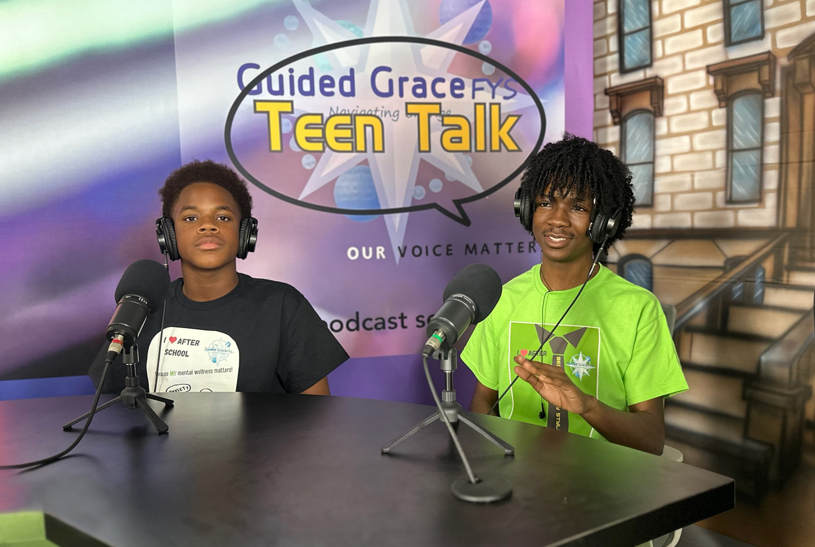 Two students sit at microphones in front of a banner that says "Guided Grace FYS Teen Talk, our voice matters" while recording a podcast.