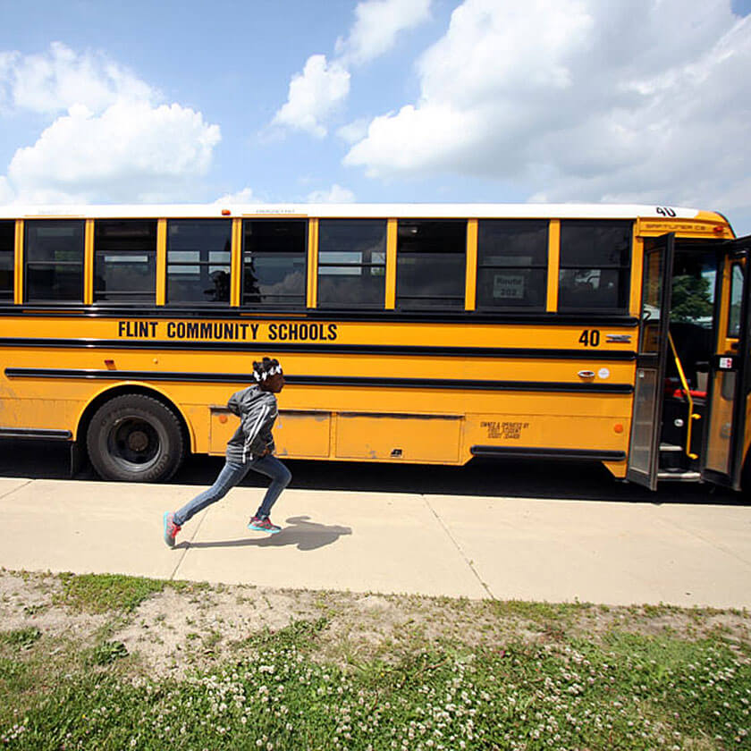 A girl runs swiftly past a Flint Community Schools bus.
