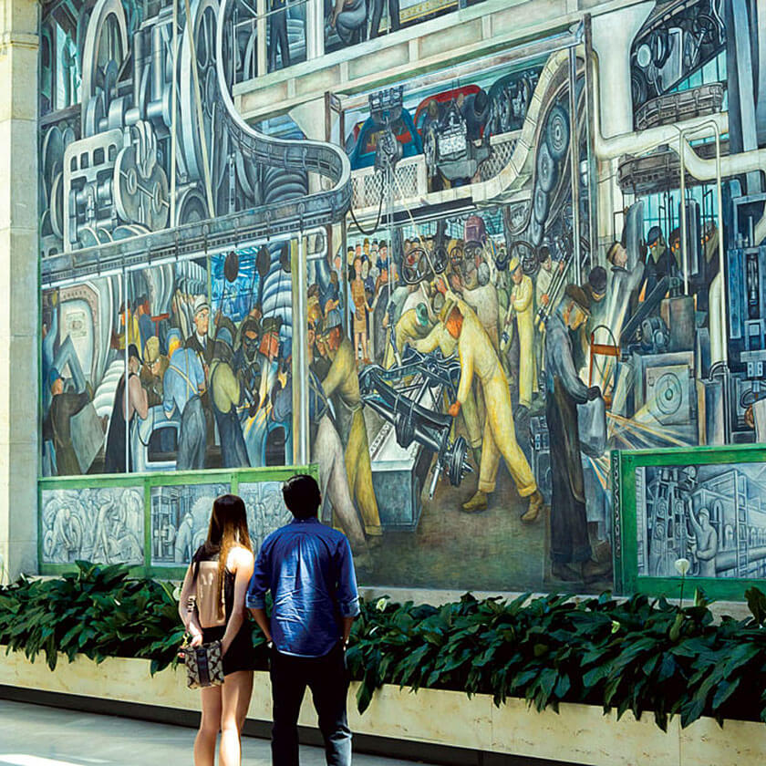 Two people look up at a Diego Rivera mural in the Detroit Institute of Arts.