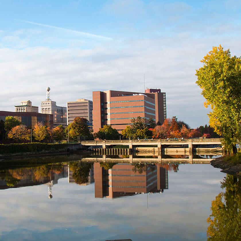 A downtown landscape is shown over a river running through the city on a sunny autumn day.