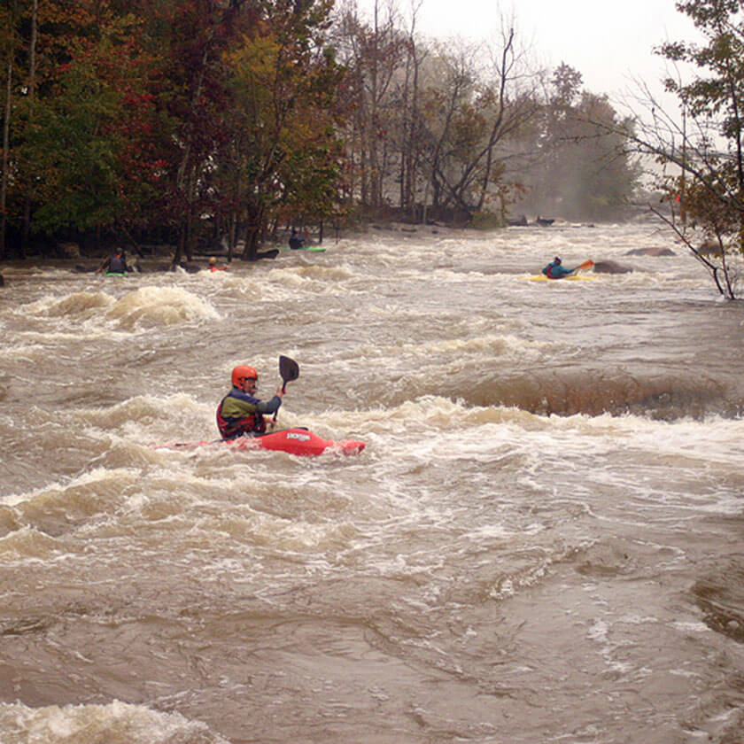 Several people canoe through river rapids.