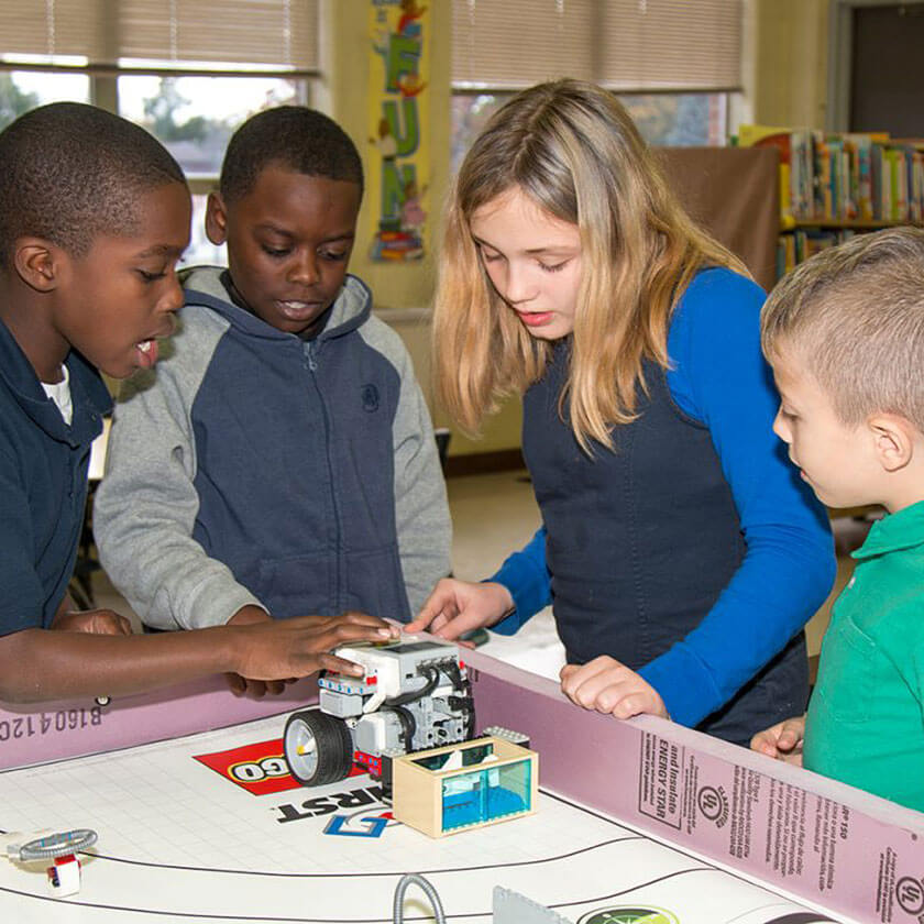 Four children play with a small robot.