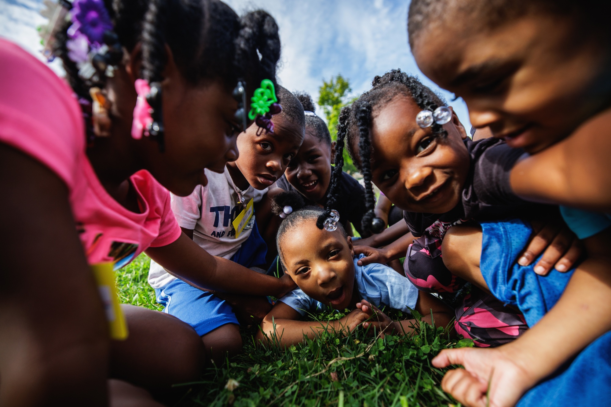 Seven kids smiling at the camera as they play on the grass.