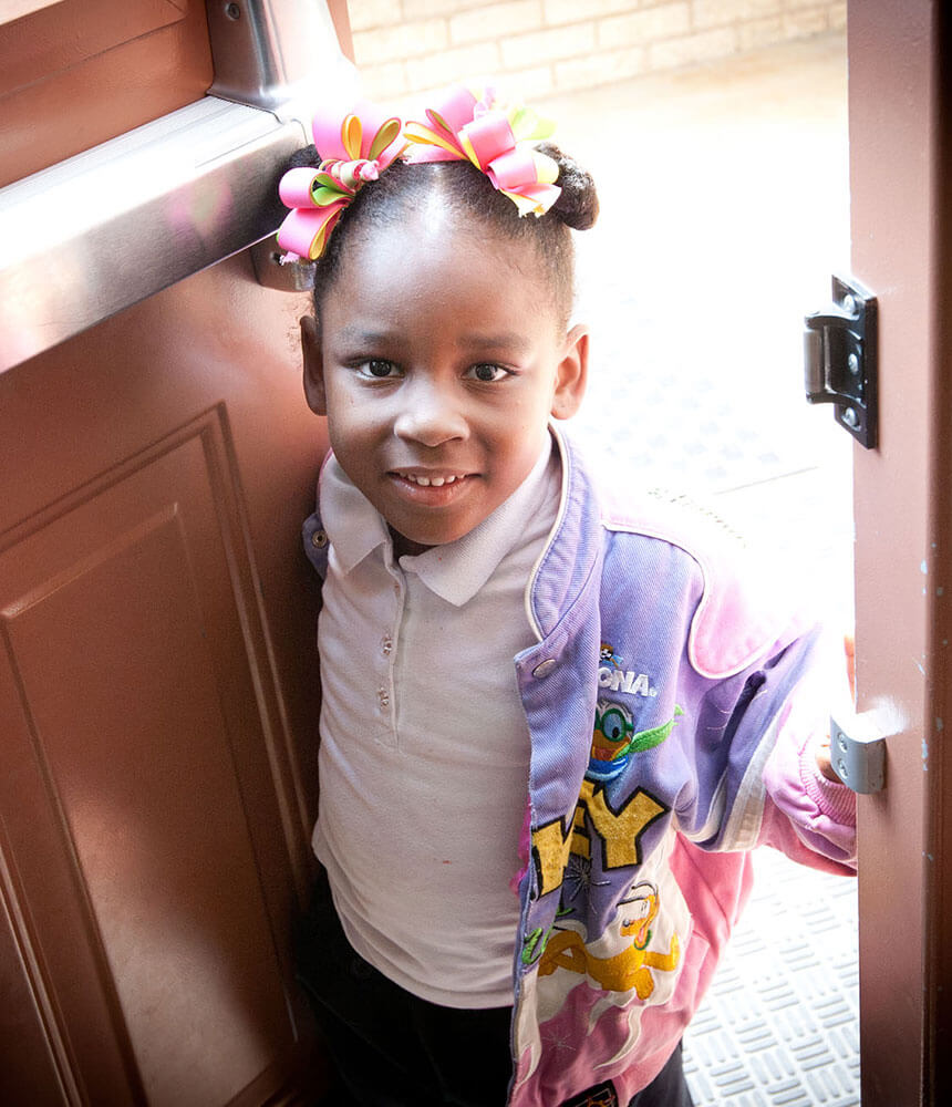 A smiling young girl enters a building through an open door.
