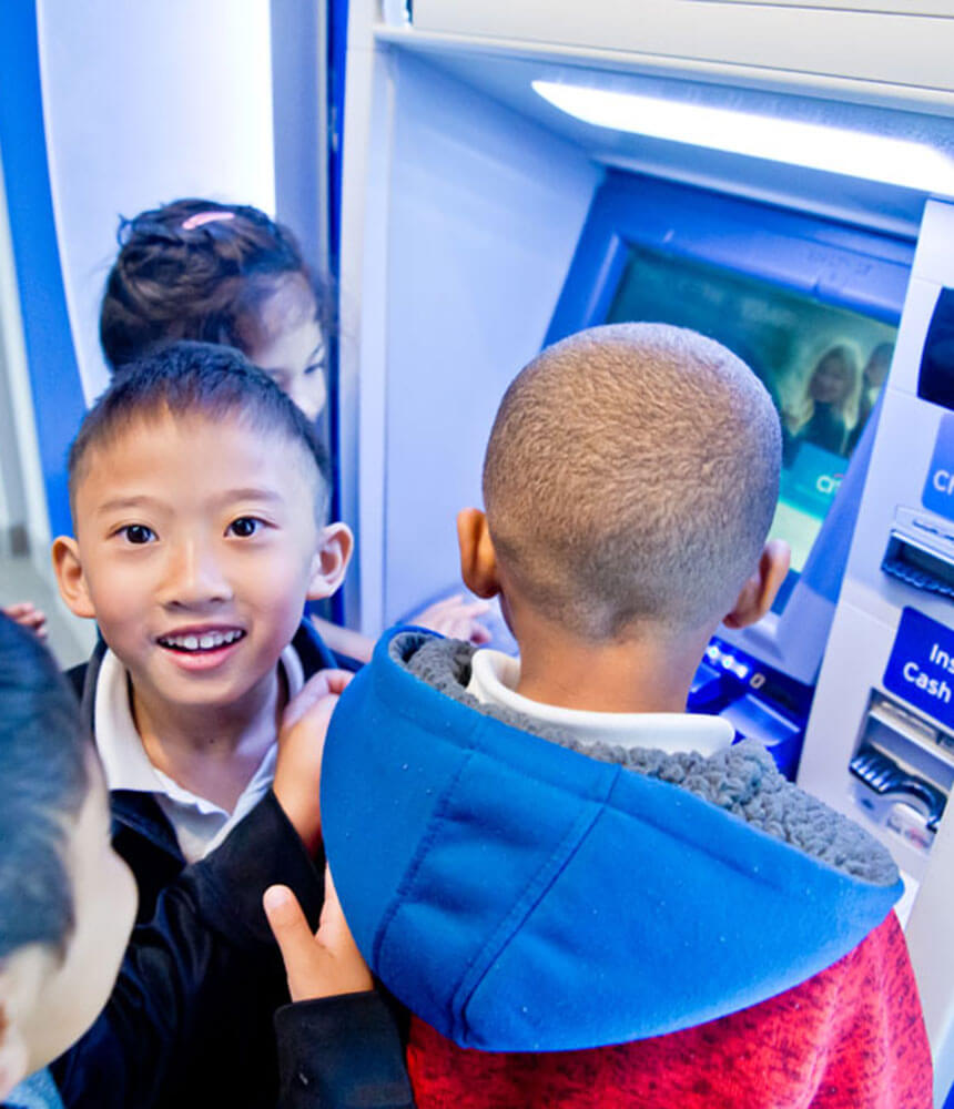 Children at an ATM deposit money into their savings accounts.