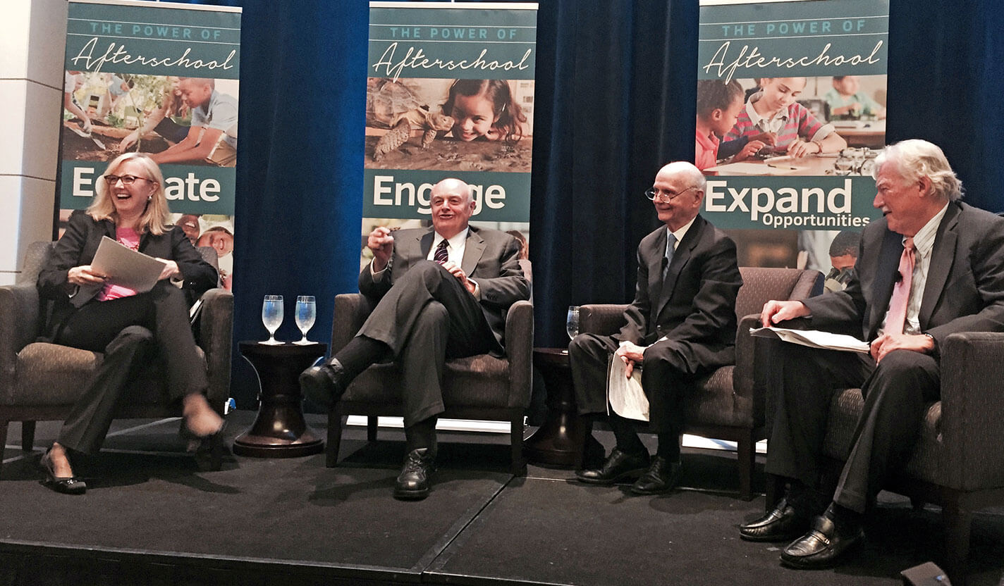 Four smiling people sit on a stage talking.