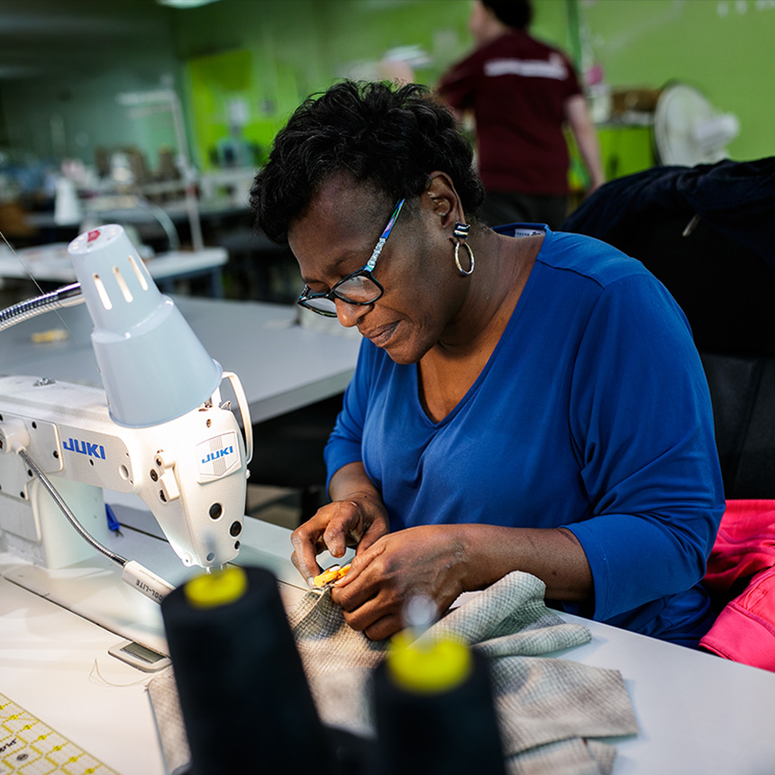 A woman works at a sweing machine and looks at the stitching work she did.